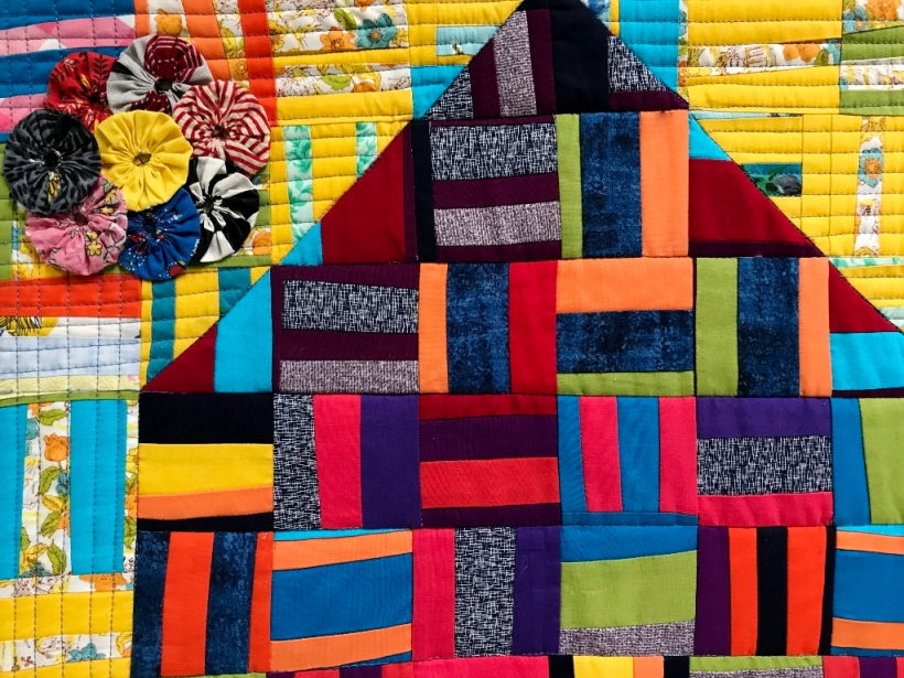 Art quilt with blocks sewn from strips of bright solid fabrics depicting a house.