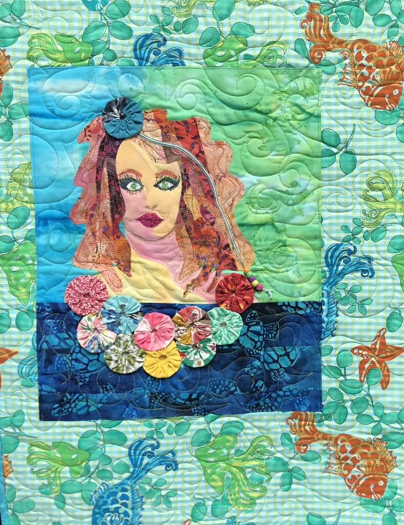 Art quilt depicting a woman's face among watery fabrics and yo-yo garland trim.