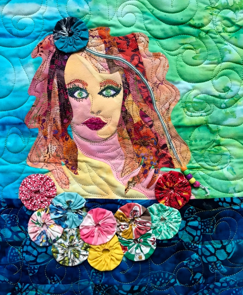 Art quilt depicting a woman's face among watery fabrics and yo-yo garland trim.