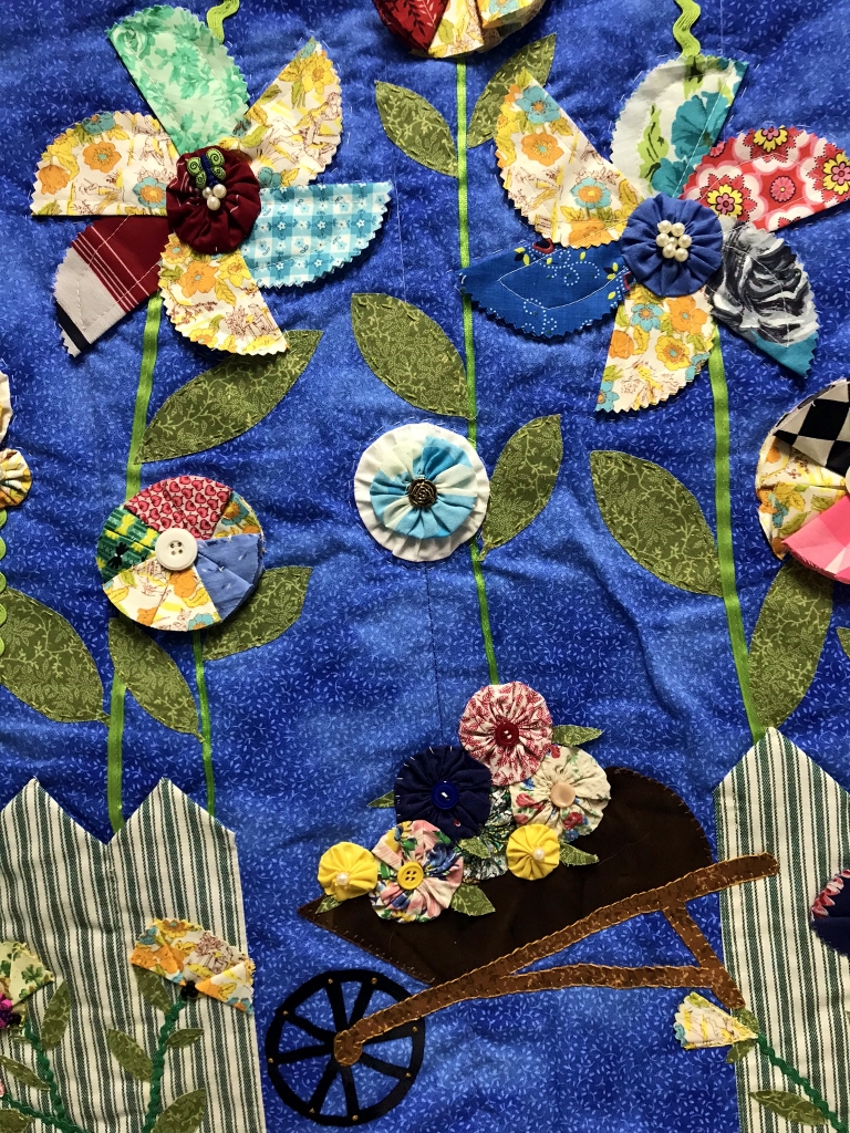 Detail of small blue quilt with garden imagery.