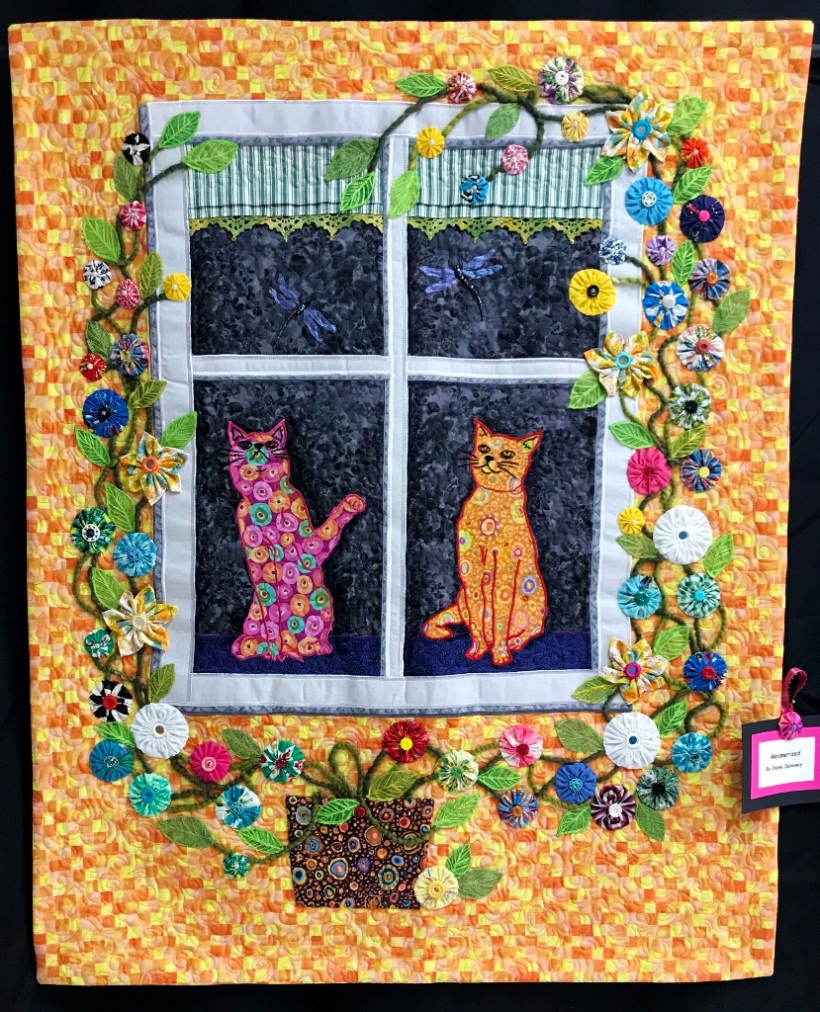 Art quilt depicting cats in a window, surrounded by flowers.