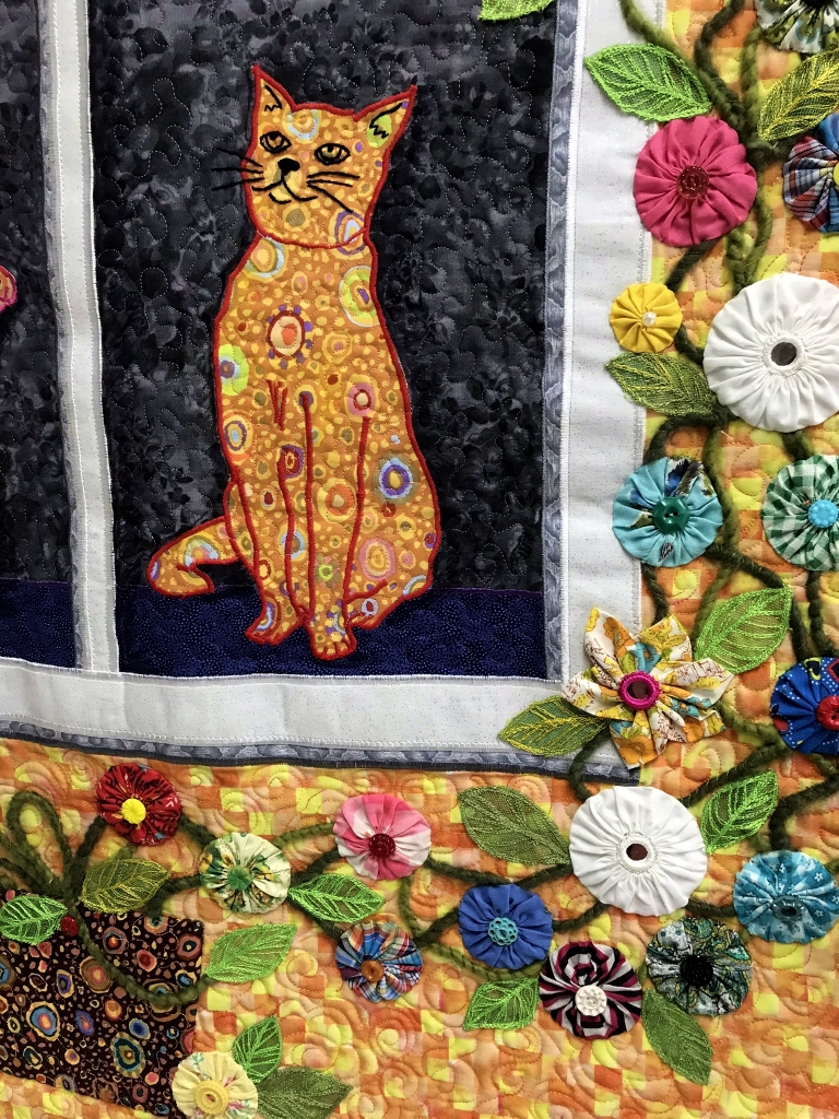 Art quilt depicting cats in a window, surrounded by flowers.