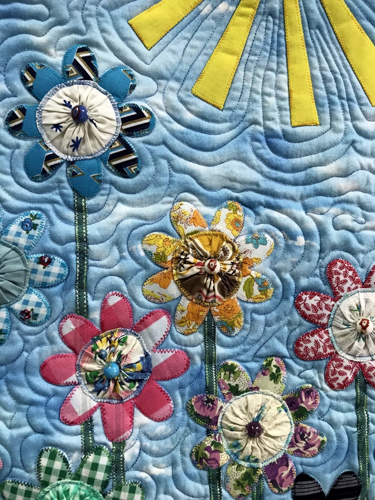 Art quilt depicting flowers under a bright yellow sun.